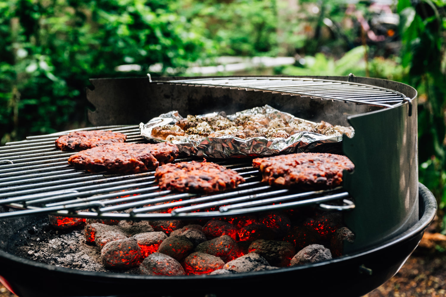 Hamburgers on grill with grilled potatoes and barbecue sauce.